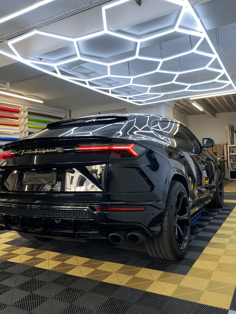 Schwarz folierter Lamborghini Urus von hinten, daneben die Folienrollen der Werkstatt