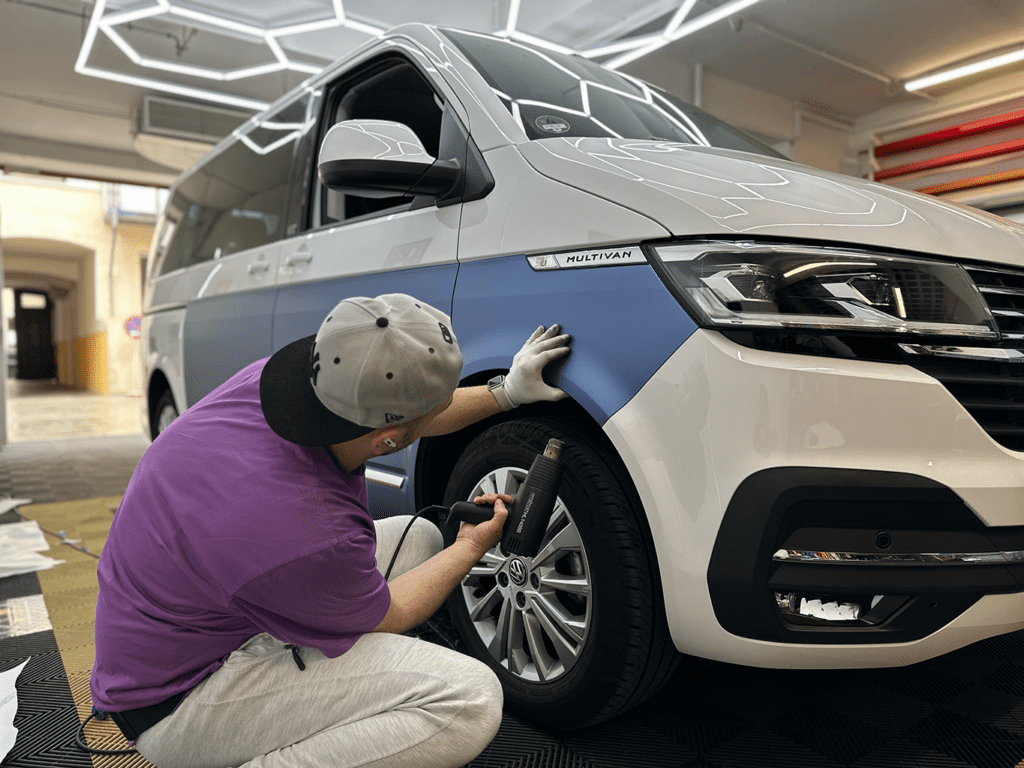 Mitarbeiter bringt Folie an der Front eines weißen VW-Transporters an