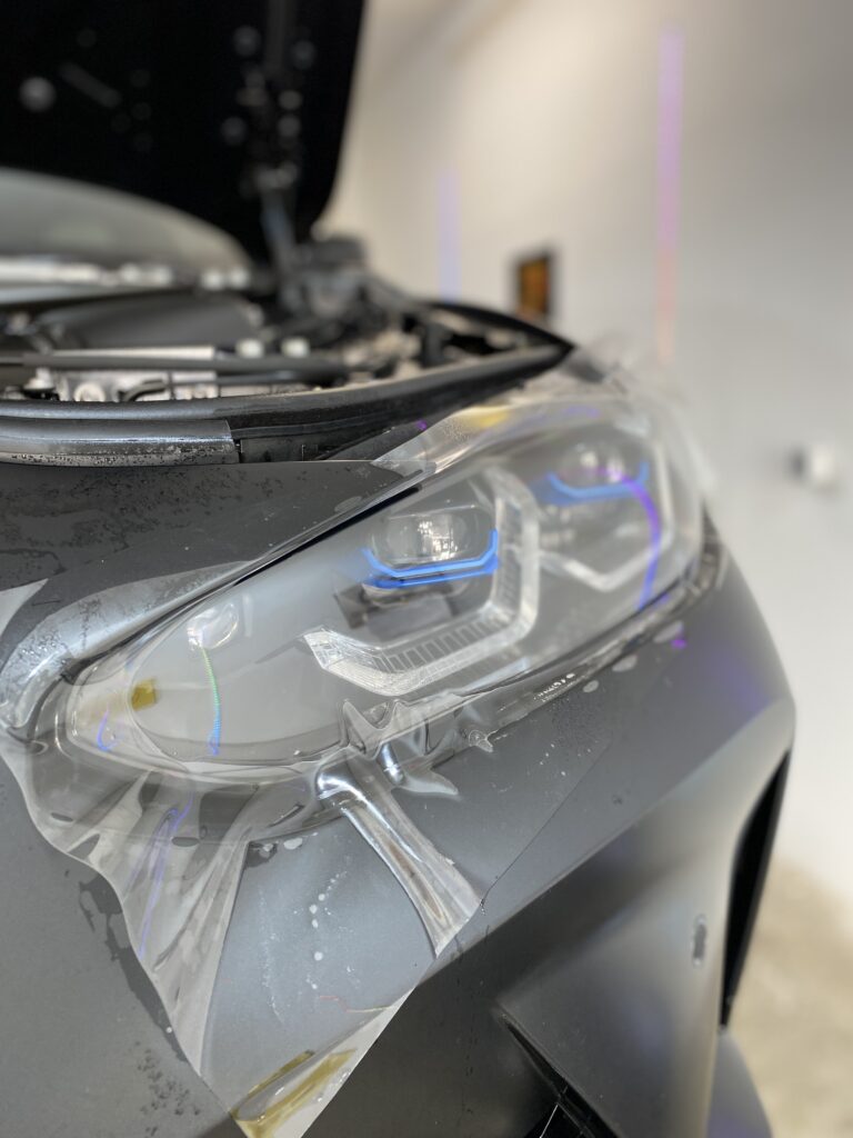 Lackschutzfolie über dem Scheinwerfer eines grauen BMW