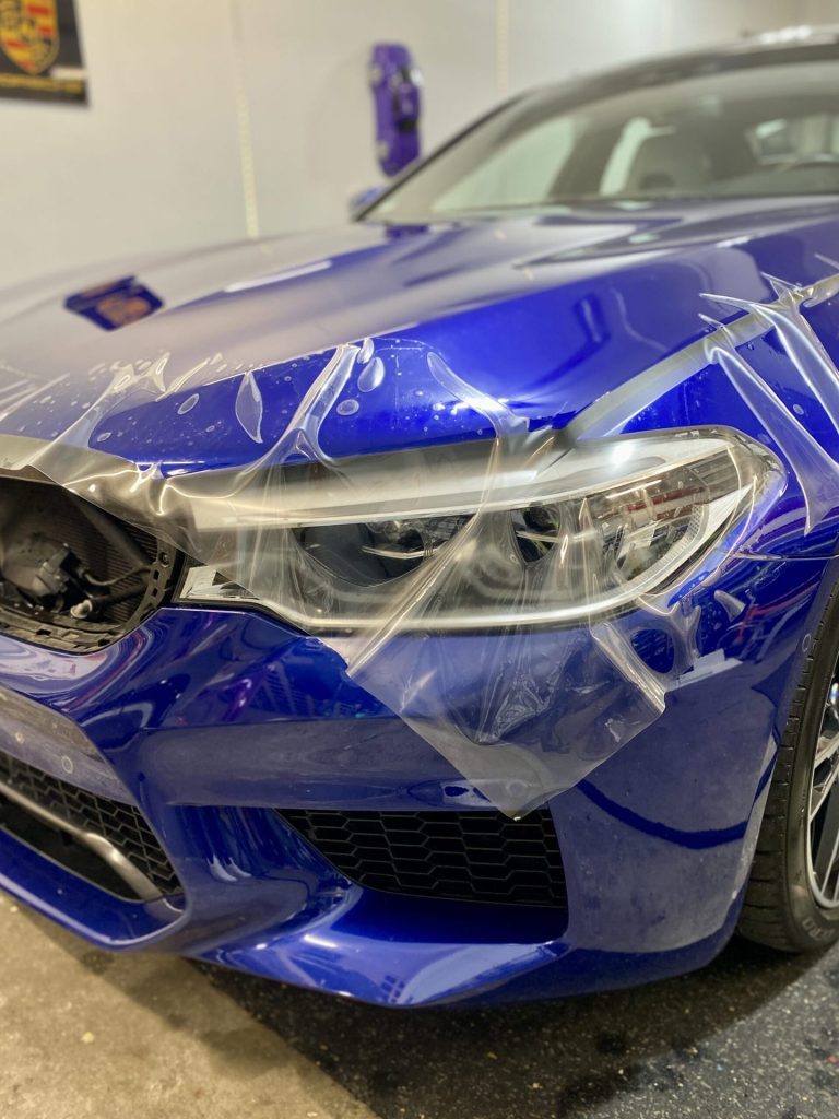Anbringen von Lackschutzfolie am Scheinwerfer eines blauen BMW