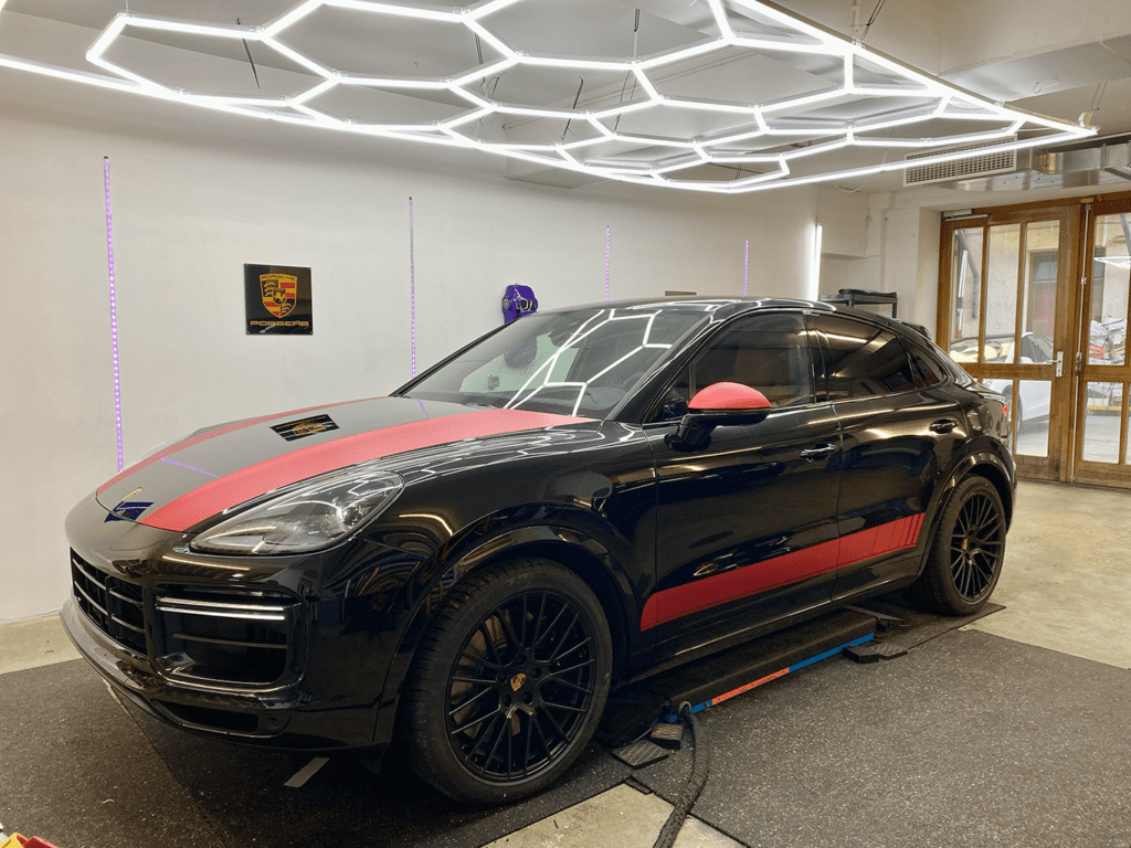 Schwarzer Porsche-SUV mit rotem Zierstreifen auf der Motorhaube unter der Hexagon-Beleuchtung