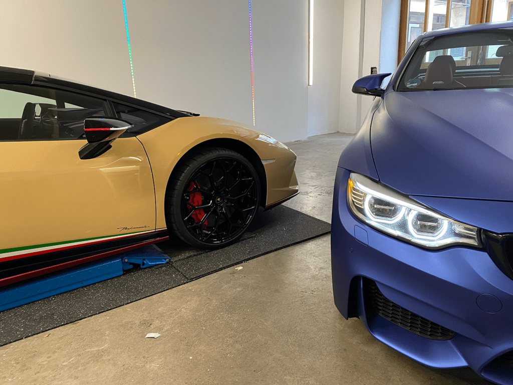 Goldfarben folierter Sportwagen neben einem mattblau folierten BMW in der Werkstatt
